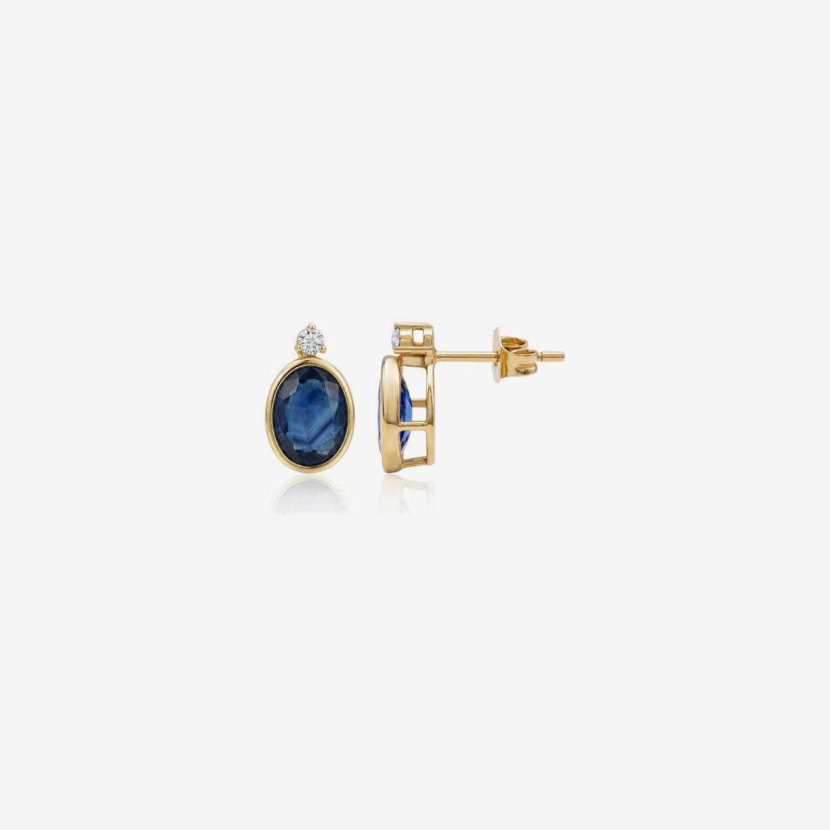 Oval Blue Sapphire Bezel Stud Earrings in 14K Yellow Gold, gray background | JJ Jewelry Miami